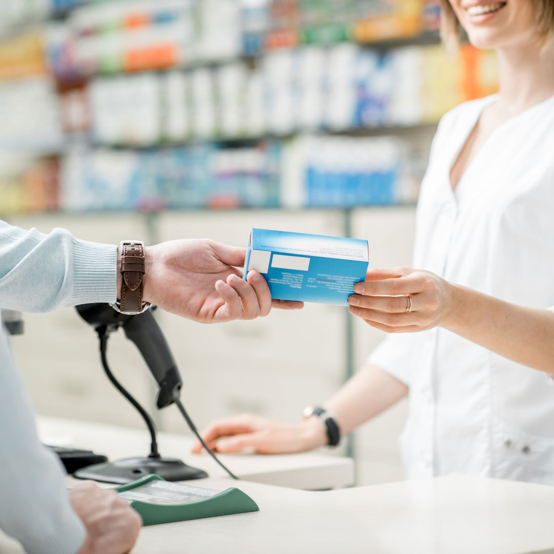 Ein Päckchen Medikament wird in einer Apotheke überreicht.