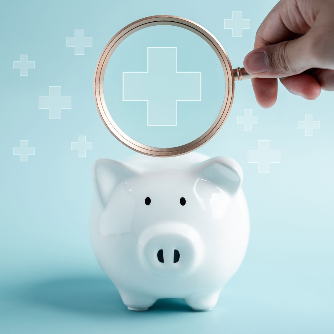 Eine Lupe vergrößert das Ambulanzkreuz über einem Sparschwein.